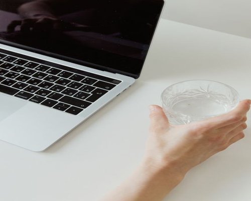 Pouring clear water into a glass next to a laptop